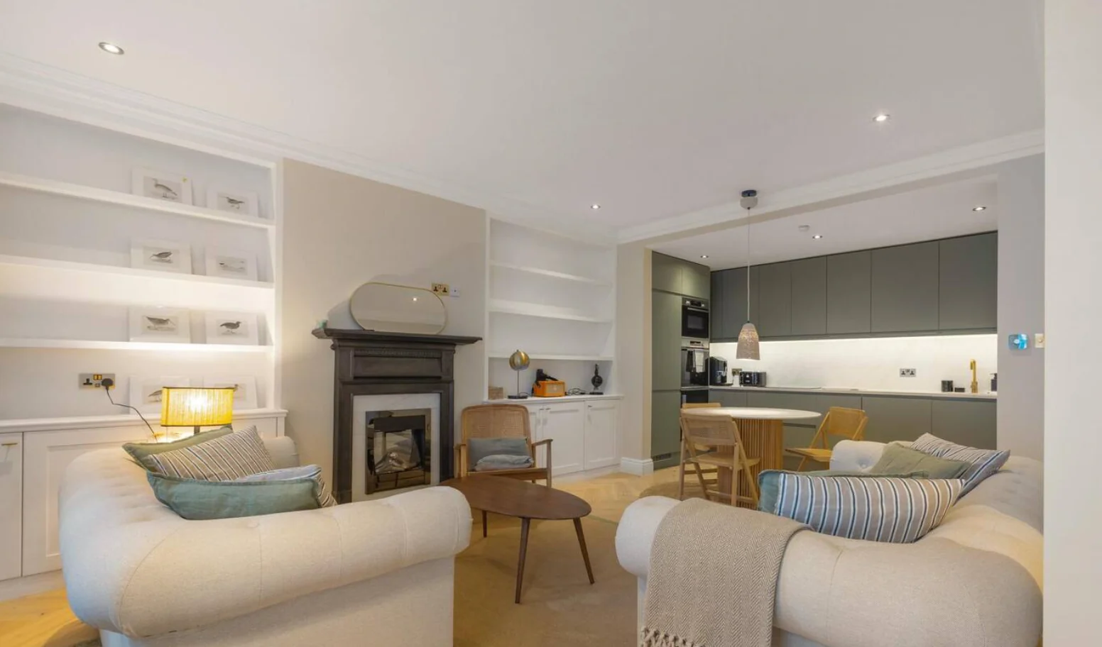 Lit alcove shelving and built-in cupboards either side of a fireplace, opening through to a bespoke kitchen, completed installation by Structure and Style Ltd